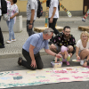 kilka osób kuca podczas malowania na planszach ulożonych na ulicy