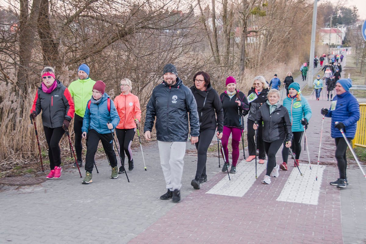 na ścieżce pieszo-rowerowej grupa osób z kijkami do nordic walking
